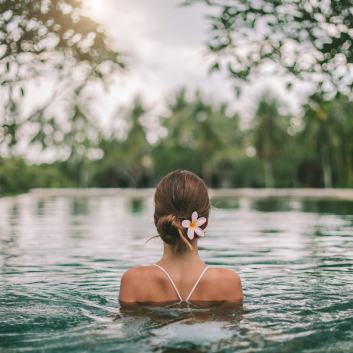 Mulher relaxa em piscina natural, com flor no cabelo, promovendo a serenidade do Retiro Tranquilo.